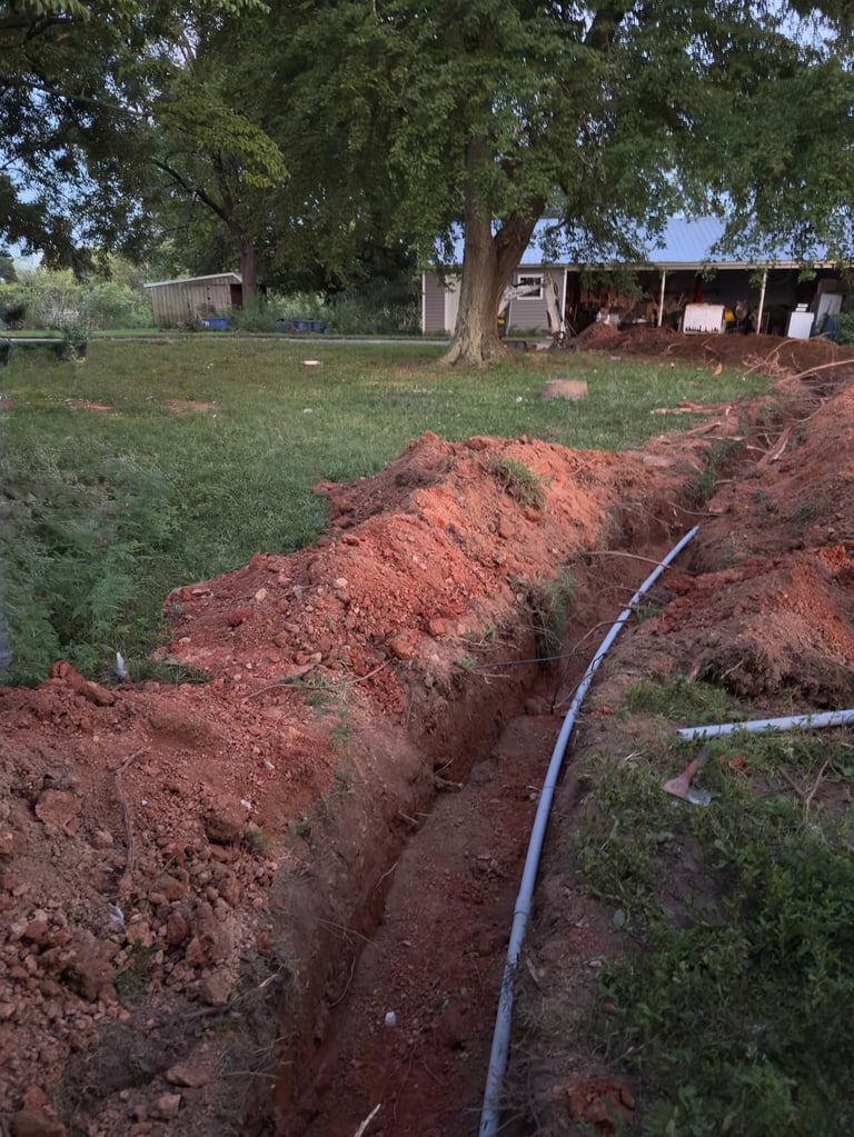 A dug trench containing a pipe leading off in the distance to a building