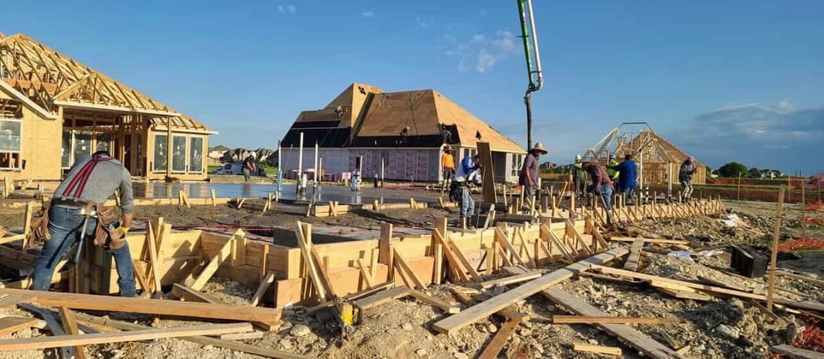 Residential construction site with multiple houses under development, wooden framing visible, and construction equipment scattered across the property