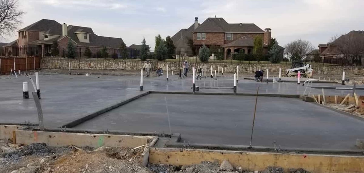 Construction site with concrete foundation poured for a building, residential homes visible in the background