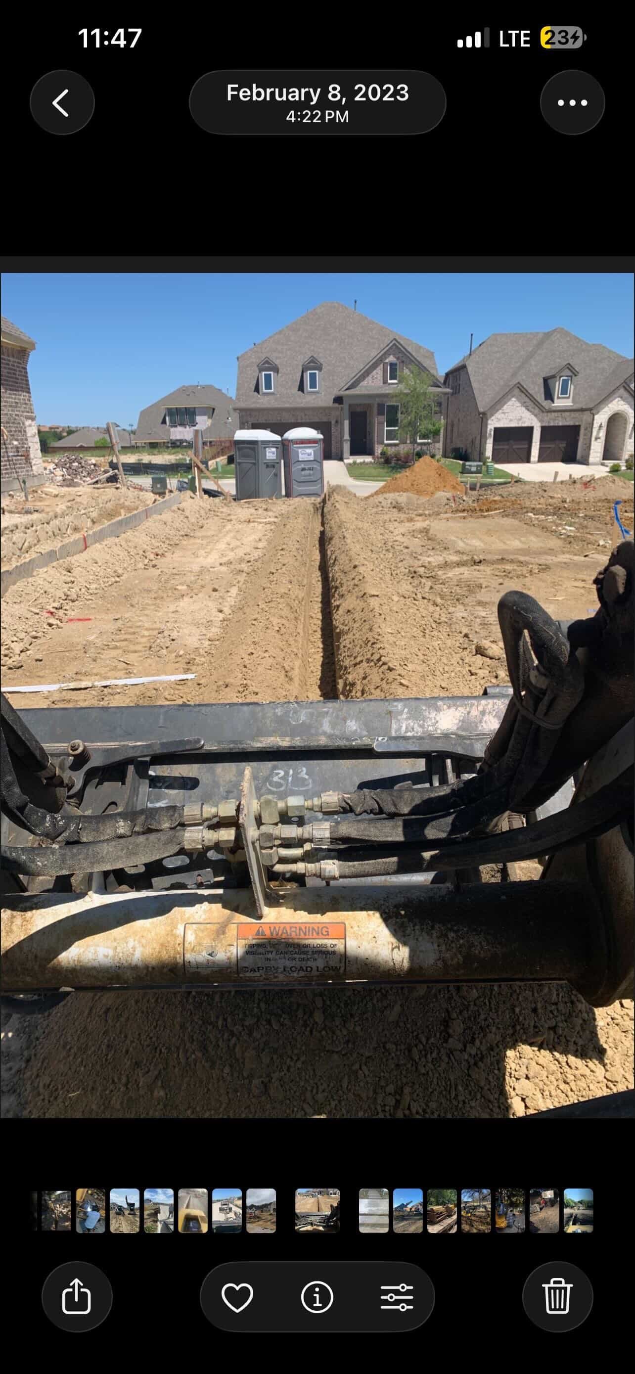 Construction site view from excavator showing two-story homes under construction with dirt yard and grading equipment in foreground